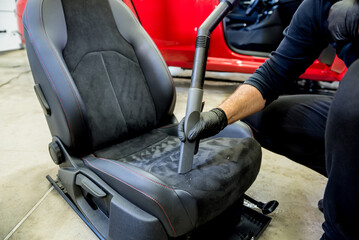 Car service worker cleaning car seat with vacuum cleaner.