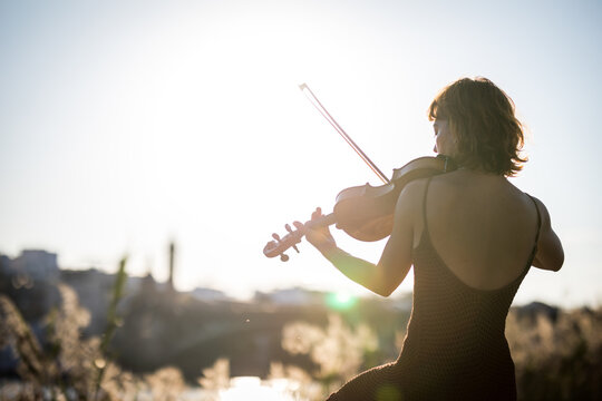 Young woman violinist posing playing on the street during sunset close up