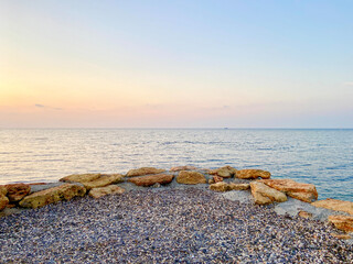 Sunset at sea. Coastline made of stones. Sunset light reflected in the water