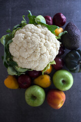 Colorful vegetables and fruits on gray textured background. Top view photo of cauliflower, apples, peach, avocado, plums. Eating fresh concept. 