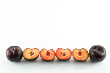 four half plums and two whole plums on a white background