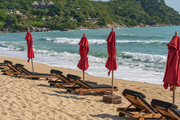 Tropical sand beach with wooden deck chairs and umbrellas near sea on a sunny day. Nature concept. Thailand