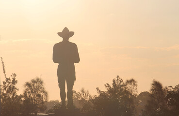 Silhouette of bushes and a Anzac monument in a soft afternoon light. The monument is an Australian...