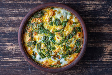 Ceramic bowl with vegetable frittata, simple vegetarian food. Frittata with egg, pepper, onion, cheese and green wild garlic leaves on table