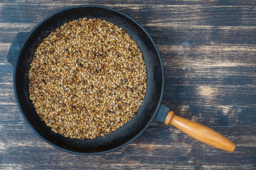 Roasted barley grains in a cast iron skillet on table, top view. Ingredient for beer or kvass