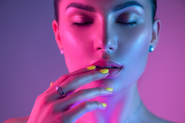 High Fashion model girl in colorful bright UV lights posing in studio, portrait of beautiful woman with trendy make-up and manicure. Art design, colorful make up. Over colourful purple background. 