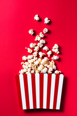 Striped Popcorn Bucket Box on Red Cinemab Background. Movies and Entertainment Concept. Flat Lay .
