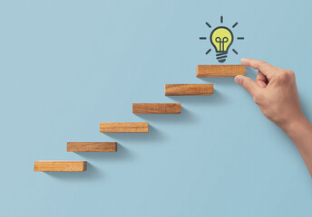Business growth, business success or career path success concept. Hand is arranging wooden blocks in a shape of staircase on blue background with light bulb icon. - obrazy, fototapety, plakaty