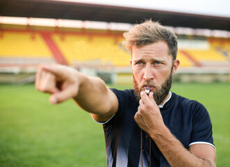 A handsome football referee with a beard plays the whistle - obrazy, fototapety, plakaty