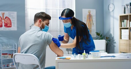 Rear of young handsome Caucasian man patient in medical mask sitting in hospital at doctors...