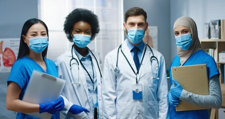 Portrait of happy young mixed-race doctors and nurses in medical masks standing in medical center...