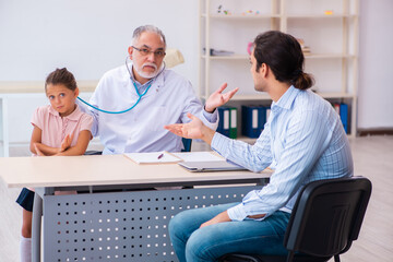 Small girl with her father visiting old male doctor