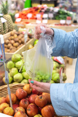 A woman holds a pack of grapes. Choosing to buy fruit in-store. Showcases with fruit i