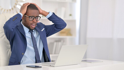 Attractive African Businessman reacting to Loss on Laptop in Office 