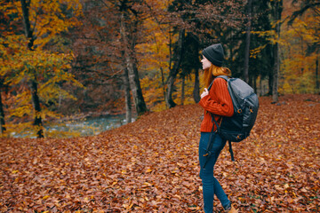 woman in a hat in a red sweater and jeans walks in the park with a backpack on her back travel tourism autumn landscape