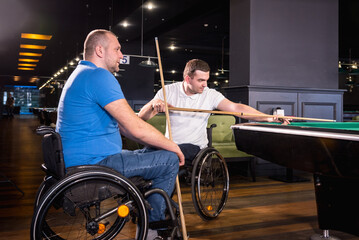 Adult men with disabilities in a wheelchair play billiards in the club