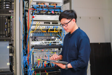 A young man using a tablet stood in the network server room while examining the server.