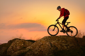 Cyclist in Red Riding Bike on the Spring Rocky Trail at Sunset. Extreme Sport and Enduro Biking Concept.