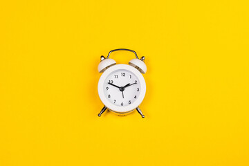 white alarm clock on yellow background. copy space. flat lay