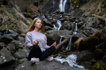 Girl sits on a tree and meditates near mountain river in Abkhazia