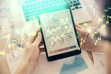 Double exposure of man's hands holding and using a digital device and forex graph drawing. Financial market concept.