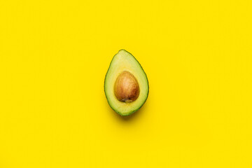 fresh ripe half of an avocado with a bone on a bright yellow background. Top view, flat lay