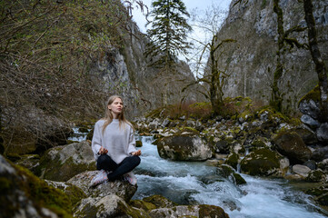 Girl sits on a tree and meditates near mountain river in Abkhazia