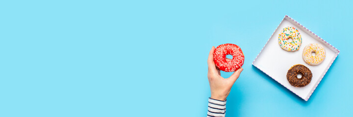 Female hand holds a donut on a blue background. Concept confectionery store, pastries, coffee shop....