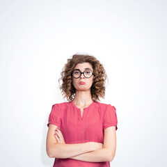 Obraz premium Young pretty girl in round glasses and in a dress with polka dots, shows an expression of strong resentment on her face, on light background. 