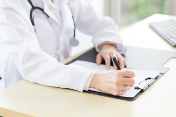 A female doctor is writing a report on a patient's condition in a hospital examination room.