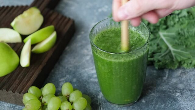 Glass of green smoothie with kale, green apple, celery, grapes and cucumber. Putting glass of vegan detox green smoothie on table, bamboo drinking straw