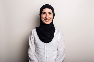 Young woman with a smile in a white shirt and hijab on a light background