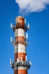 Factory chimney (brick tube) with mobile antennas against blue sky