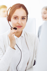 Call center in sunny office. Group of diverse operators at work. Beautiful woman in headset communicating with customers of telemarketing service