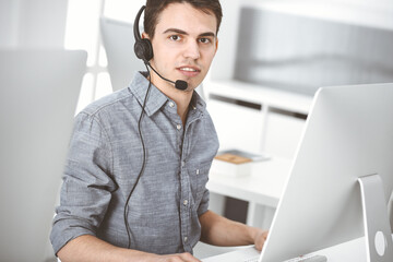 Casual dressed young man using headset and computer while talking with customers online. Call center, business concept