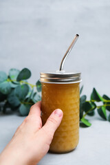 Sustainability, healthy eating concept. Female hand holding fresh fruit juice in takeaway glass with metal straw. Reusable glass packaging for beverage. 
