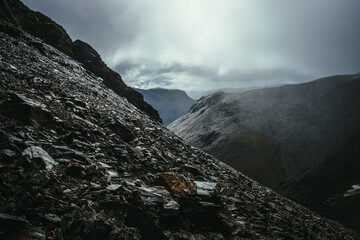 Dark atmospheric landscape on edge of abyss in highlands. Dangerous mountains and abyss in overcast weather. Danger mountain pass and sharp rocks under gray sky. Dangerous rainy weather in mountains.