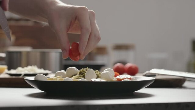 Slow motion orbit shot of man add cherry tomatoes to pesto penne on black plate