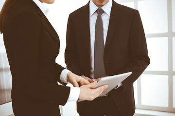 Businessman and woman using tablet computer for discussing questions in office. Partners or colleagues at meeting. Business cooperation concept