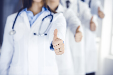 Group of modern doctors standing as a team with thumbs up in hospital office. Medical help, insurance in health care, best desease treatment and medicine concept