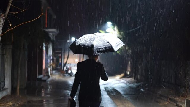 In the rainy night, a man is walking on the path home with an umbrella.