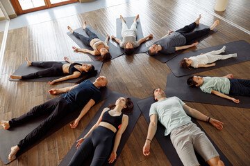 View of a big group of young people laying on yoga mat in a circle, stretching in a yoga class