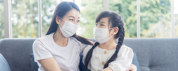 Mom and young girl kid wearing face mask at home Mother looking at daughter sitting on sofa