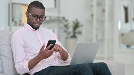 African Man using Smartphone and Laptop at Home 