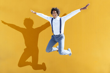 Fototapeta na wymiar Black man with afro hair jumping on a yellow urban background