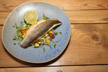 A delicious plate of fish Sea Bass with Mango and Avocado Salsa on a wooden kitchen table