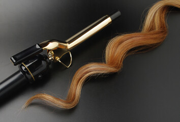 Professional Hairdressing Curling Iron With A lock Of Waved Hair on A Black Background, Spotted...