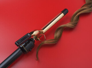 Professional Hairdressing Curling Iron With A Lock Of Wavy Hair On A Red Background, Spotted With Ray Of Lights