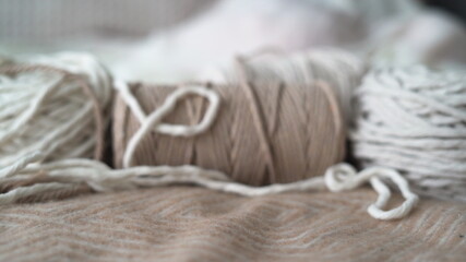 Boho-style wool threads are lying on the bed, a woman's hand is laying a ball. Suitable for macrame, banners and craft advertisements.