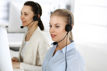 Blond woman call operator is using computer and headset for consulting clients online. Group of diverse people working as customer service occupation. Business concept